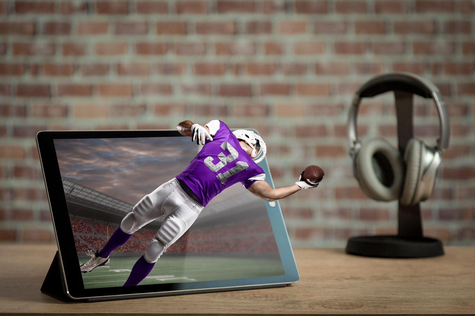 Trójwymiarowy model zawodnika futbolu amerykańskiego w fioletowym stroju wychodzący poza ramy ekranu tabletu co demonstruje nowoczesne animacje 3d i efekty przestrzenne