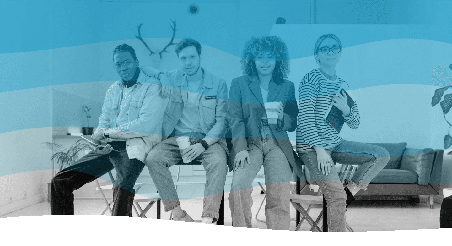 A group of four diverse individuals are seated casually together in a modern living room, featuring a stylish sofa, abstract wall art with antlers, and lush green plants, each holding a cup as they sit on stools.
