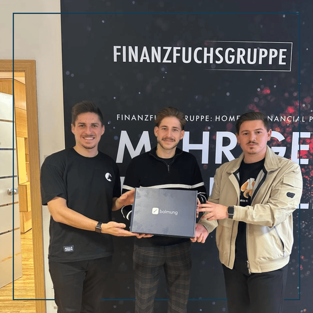 Drei Männer stehen vor einem Banner und halten stolz eine balmung Plakette