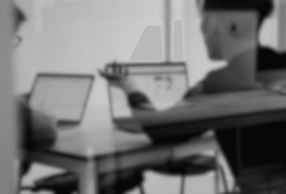 Black and white image of people working at a table with laptops, showing hands gesturing during discussion of digital content displayed on screens, with fabrica® logo in the corner.