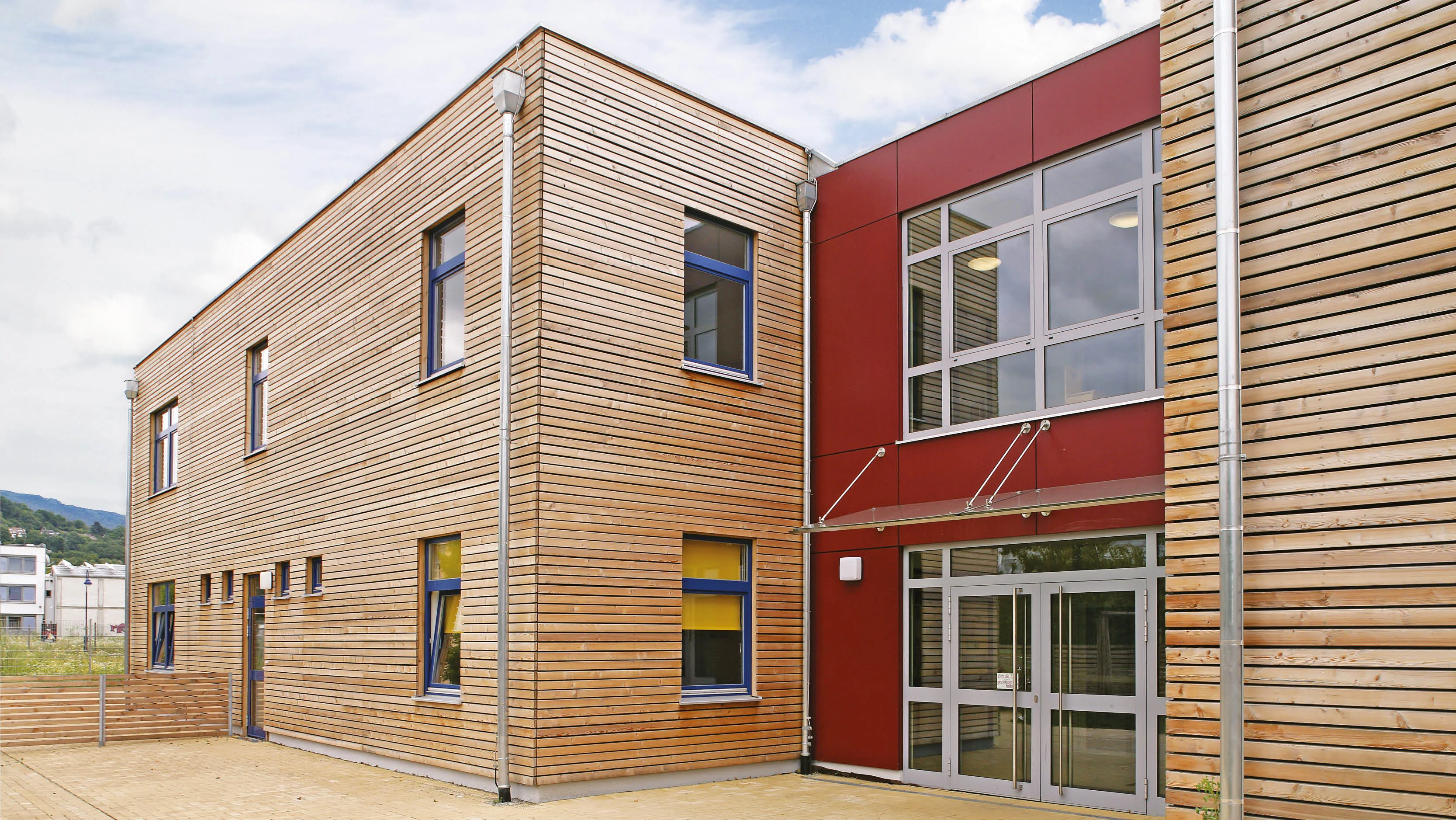 Moderne Holzfassade und rote Verkleidung eines Gebäudes mit großen Fenstern und Glastüren.