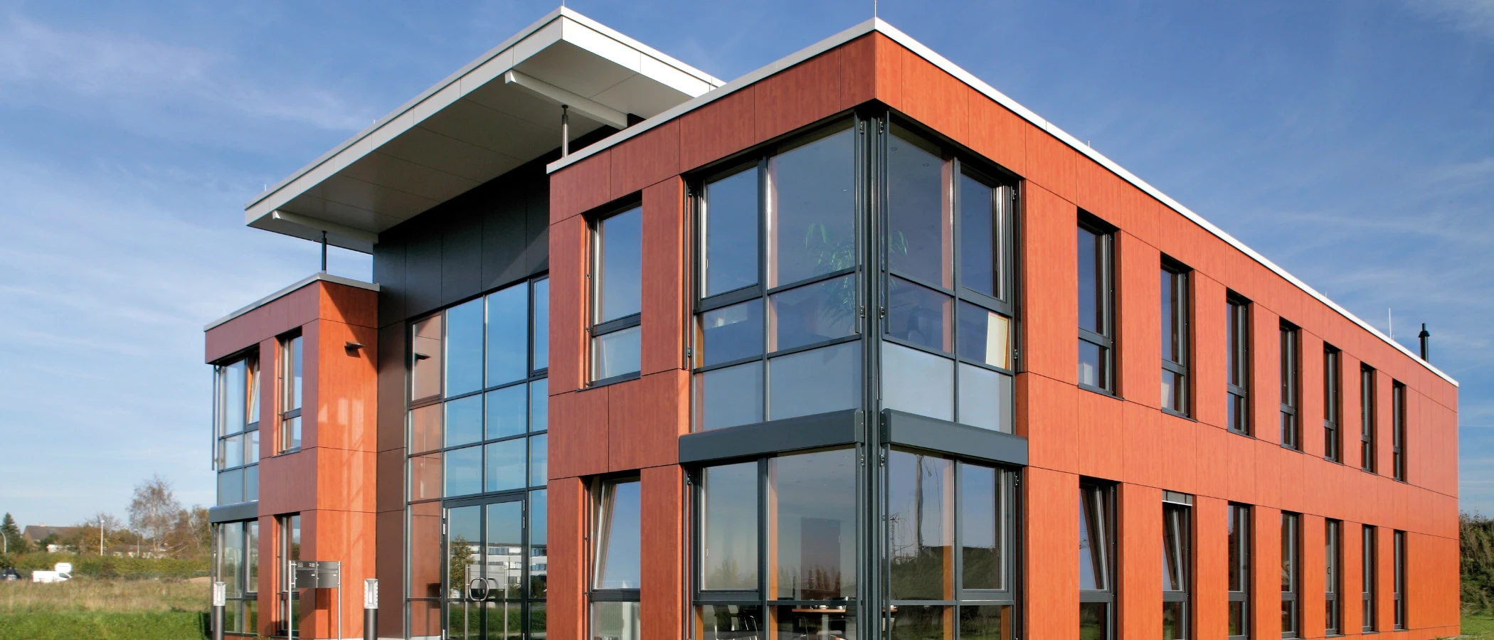 Modernes Bürogebäude mit orangefarbener Fassade und großen Glasflächen im blauem Himmel.
