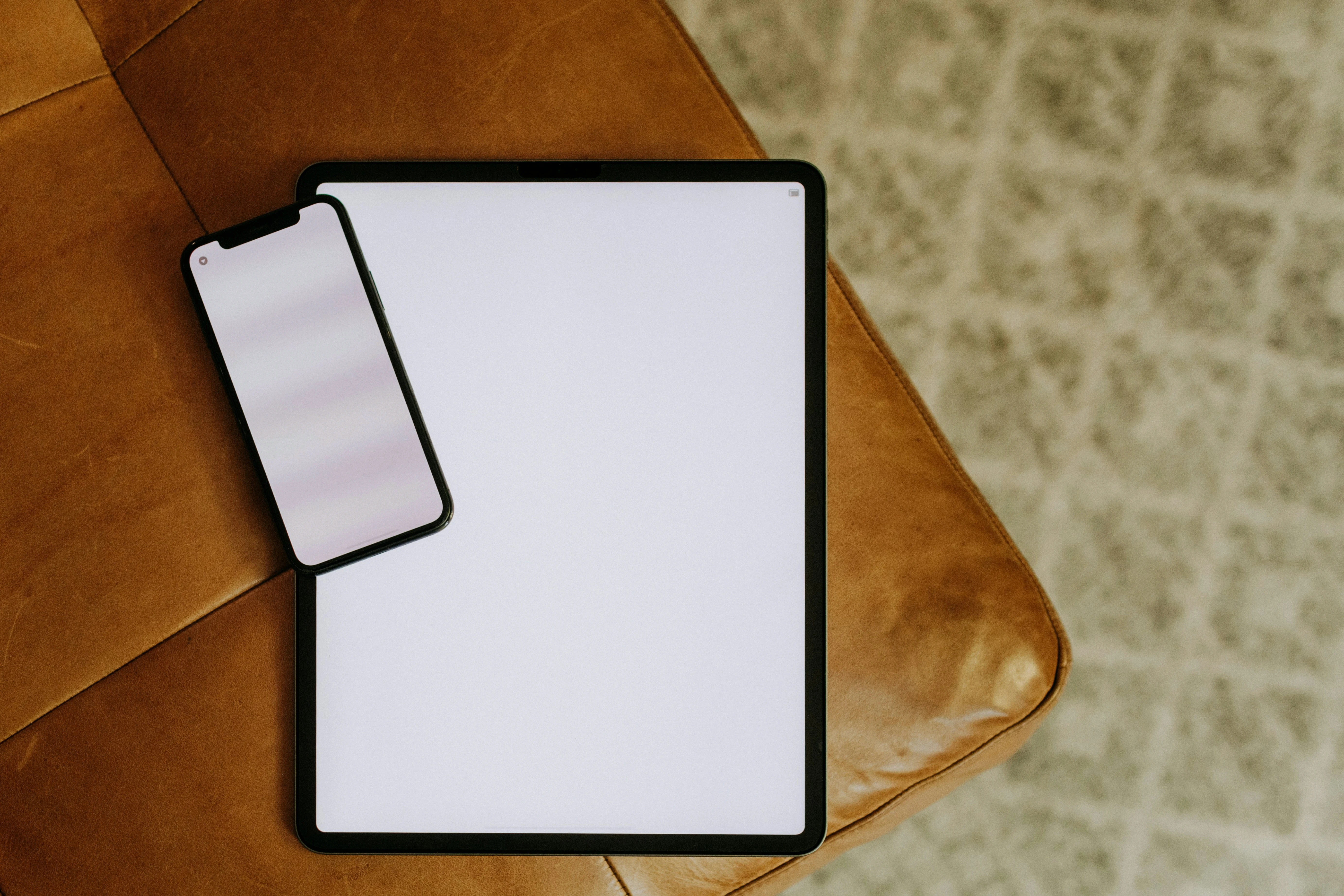 iPad next to a smartphone on a brown leather chair, both screens blank.