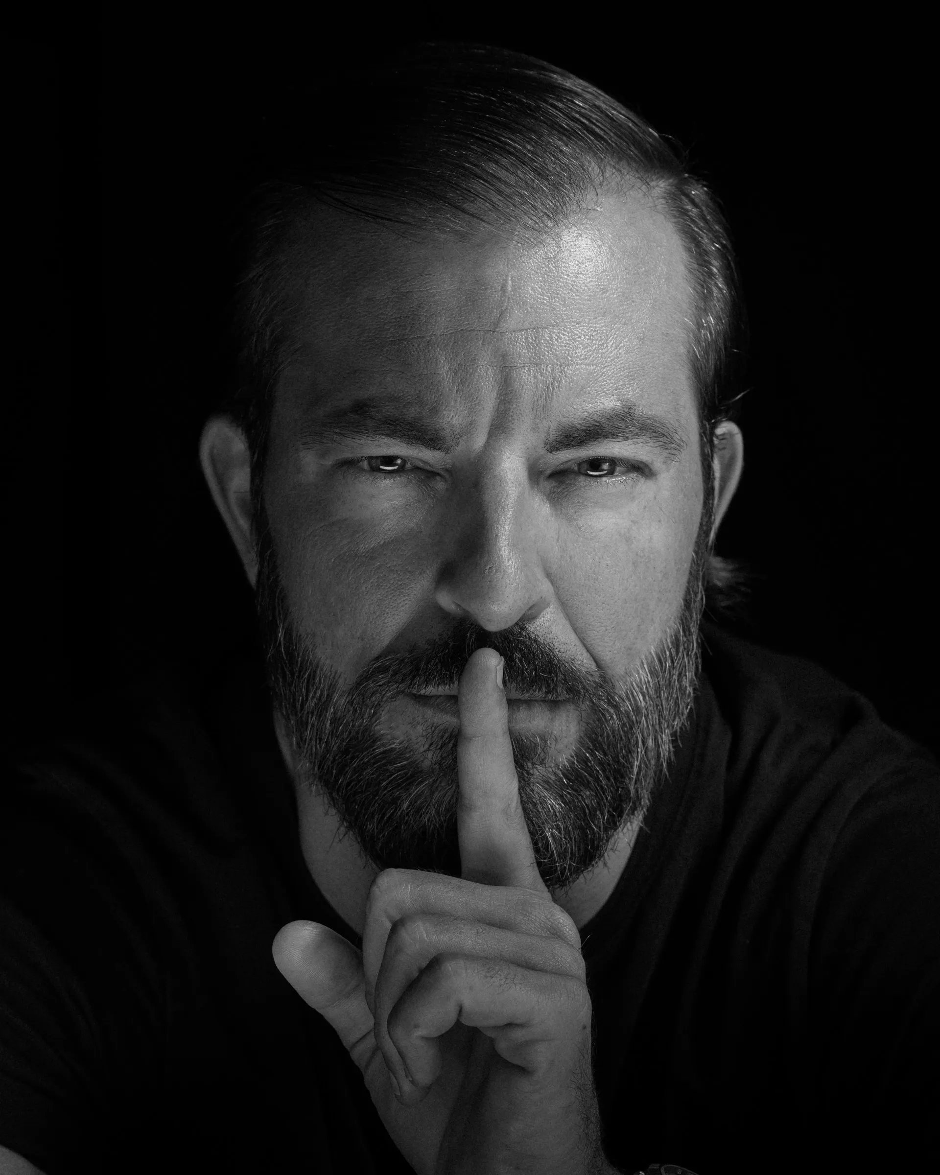 Black and white portrait of Swiss artist Bligg making a quiet gesture with his finger to his lips.