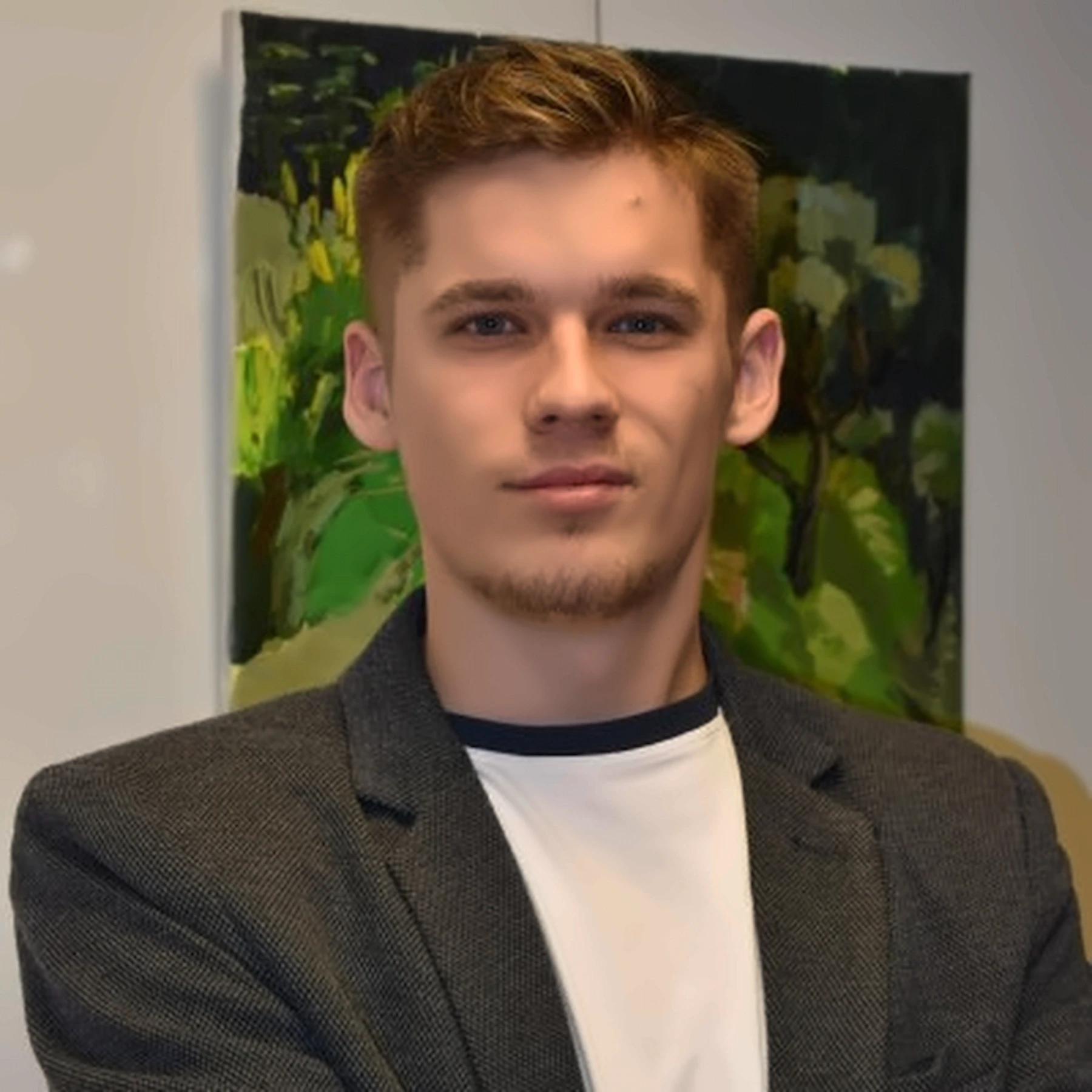 Young man in a suit jacket and white t-shirt, looking at the camera. Abstract painting in the background.