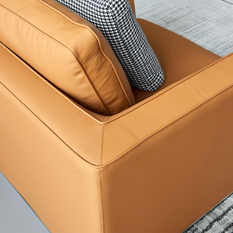 Modern tan orange faux leather or genuine leather sofa detail: boxed arm, stitched seams, cozy black-white checkered cylindrical pillow, contemporary furniture texture