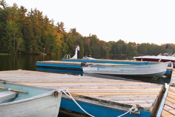 Newlywed couple sharing a romantic kiss on a rustic wooden dock, surrounded by the serene waters and lush greenery of Muskoka.