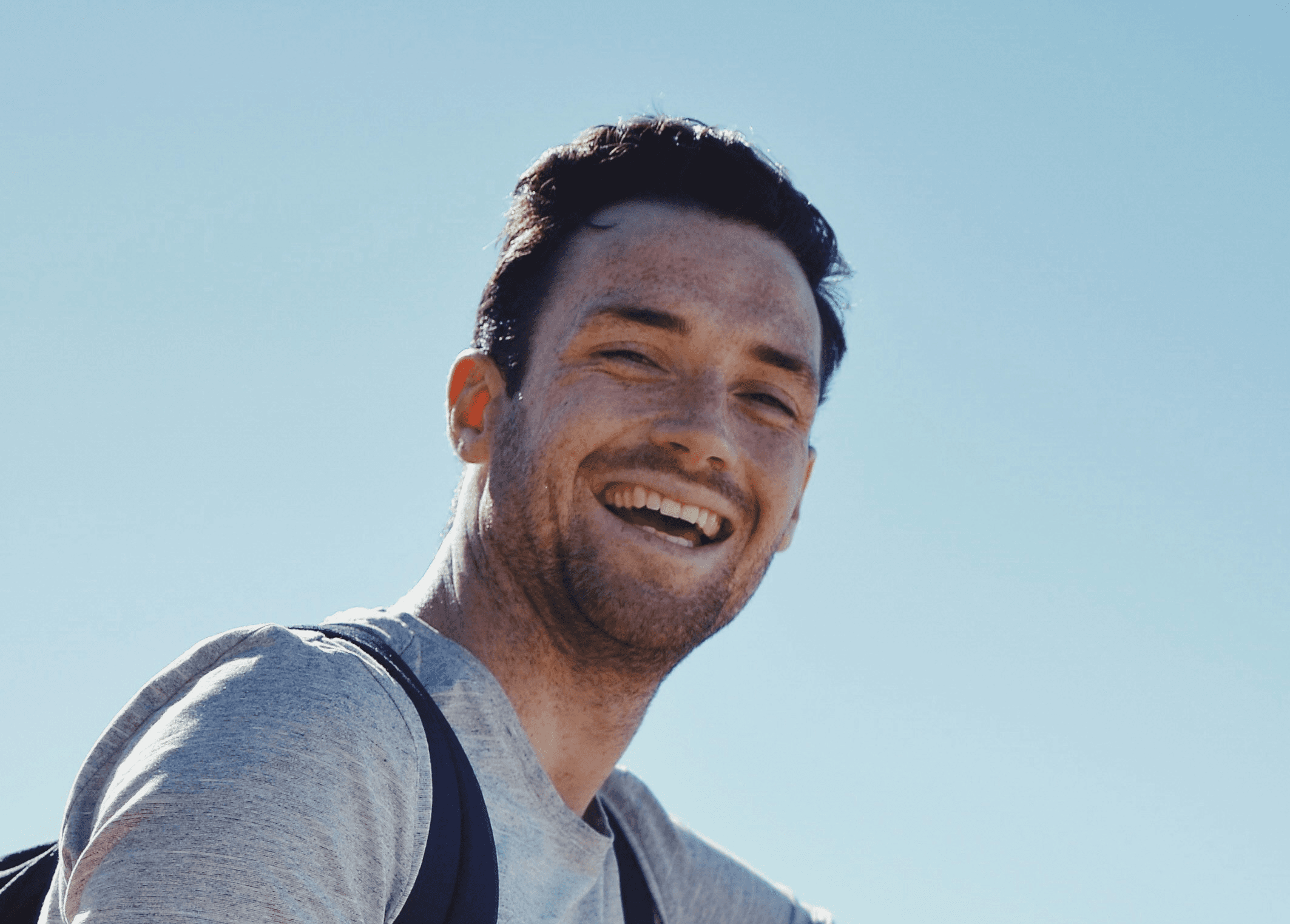 smiling man sitting on gray rock at daytime