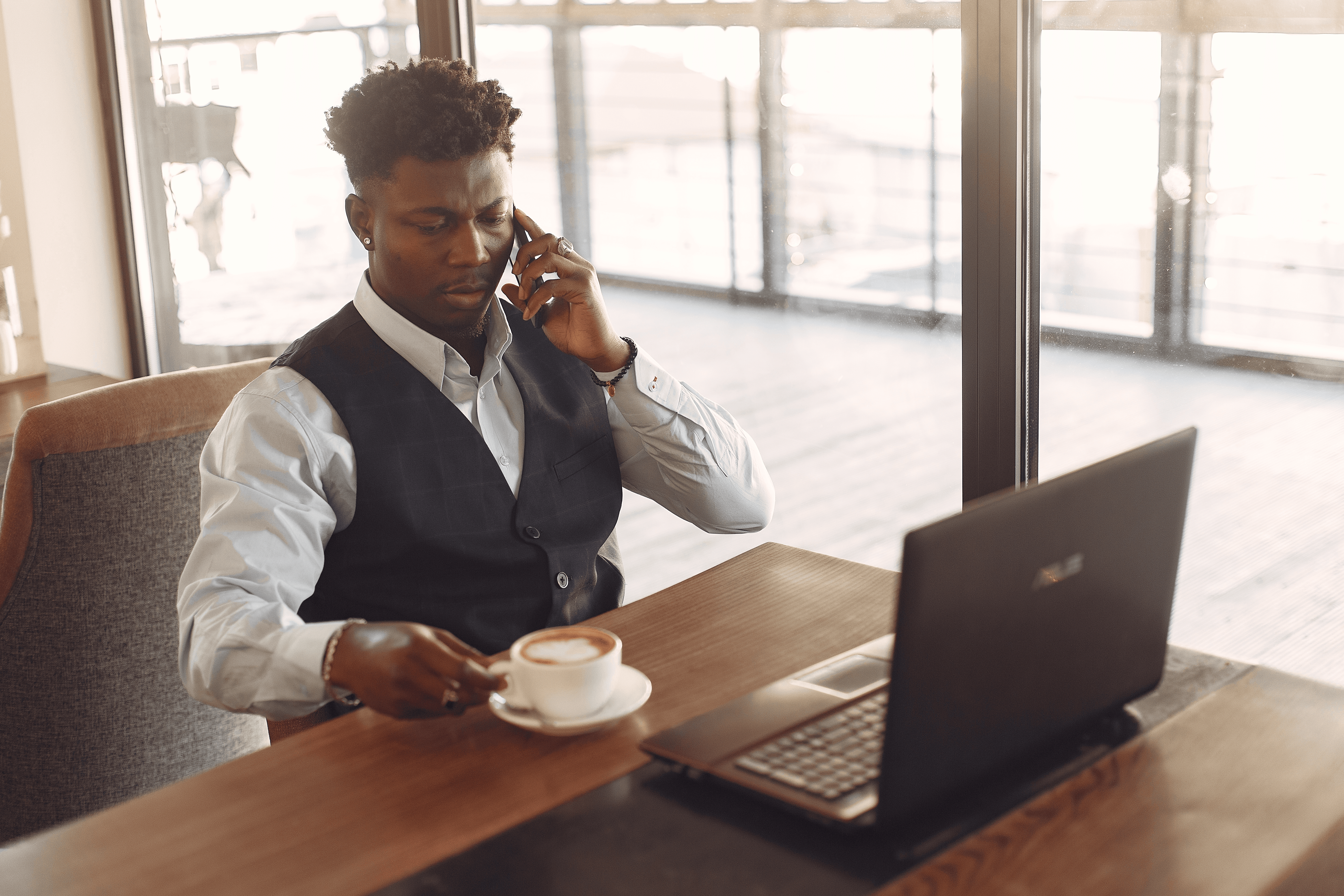 A woman sitting at a desk in a bright office, working on a laptop with notebooks, a cup, and a desk lamp beside her.