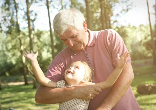 Grandfather hugging his granddaughter in the park, smiling and enjoying the sunlight together.