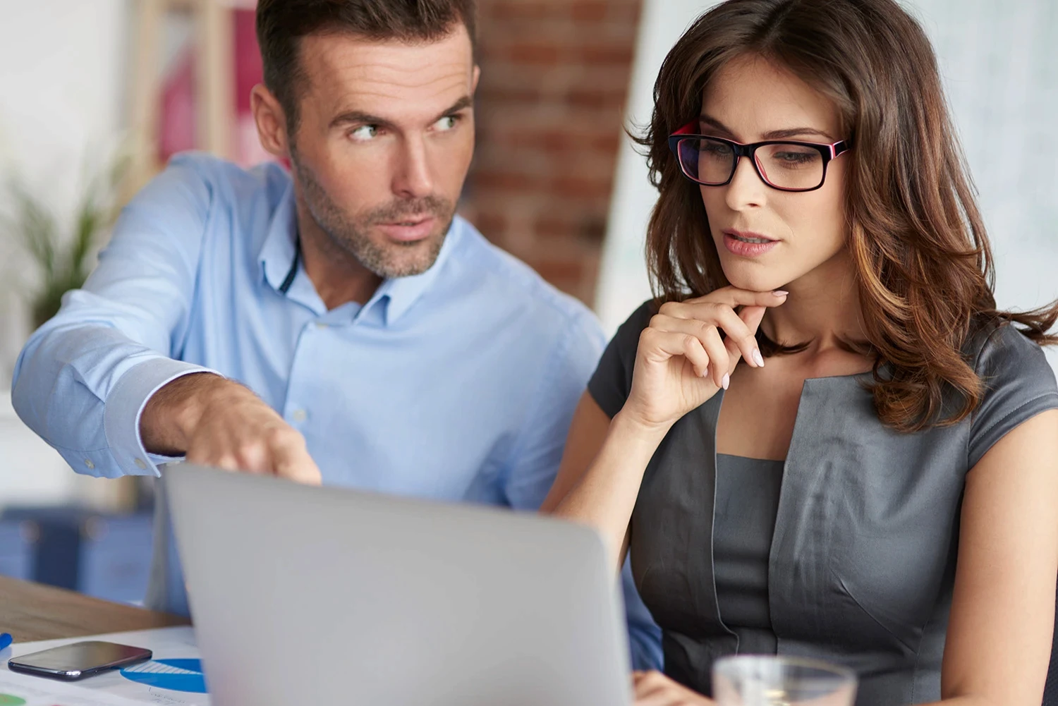 Man pointing at important information on a computer screen while a woman looks thoughtfully.