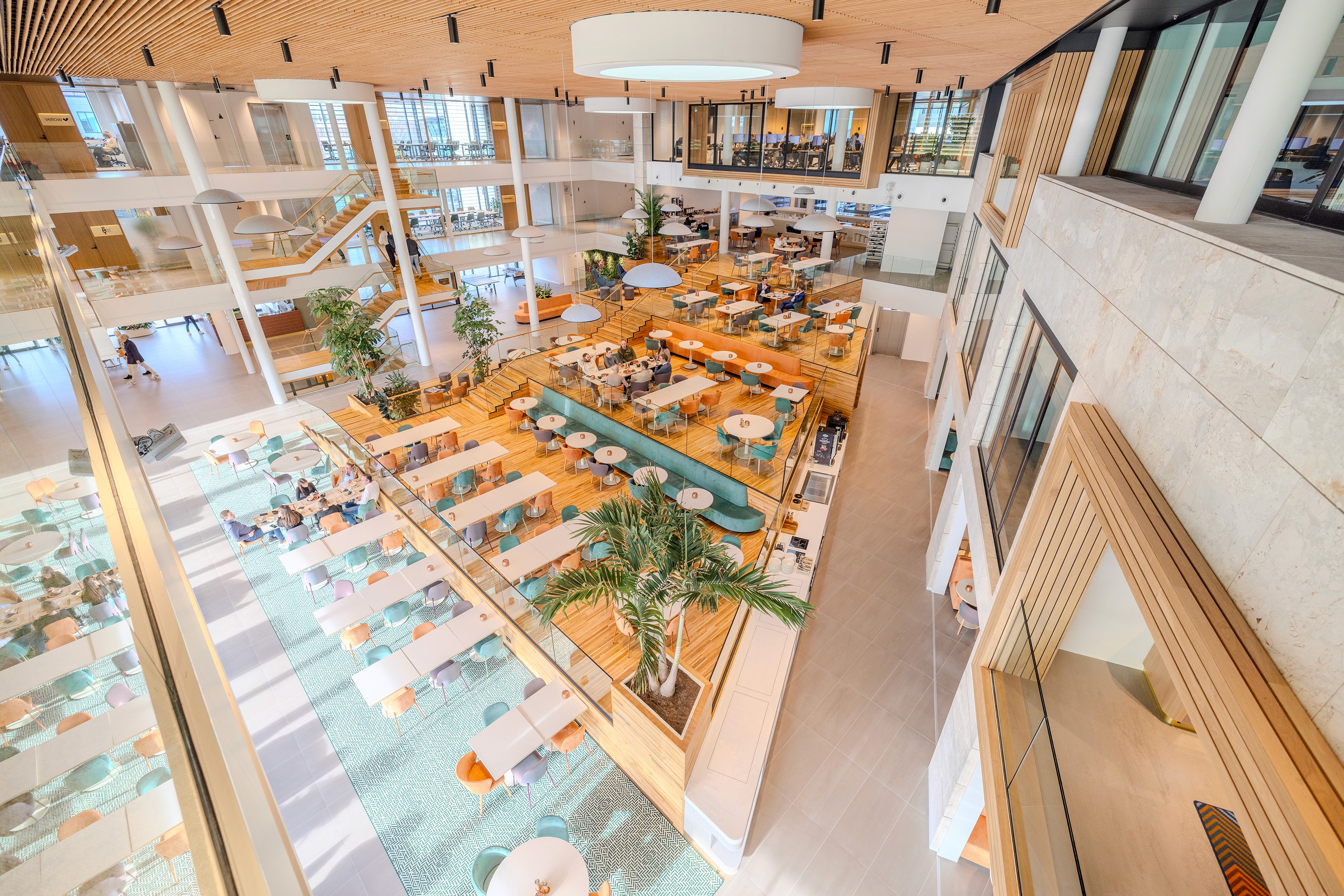Vogelvluchtperspectief van het atrium in AFAS DotNL, Leusden – open kantoorruimte met loungetafels, groene planten en lichte houten vloer, ingericht door DSN Workspace Solutions