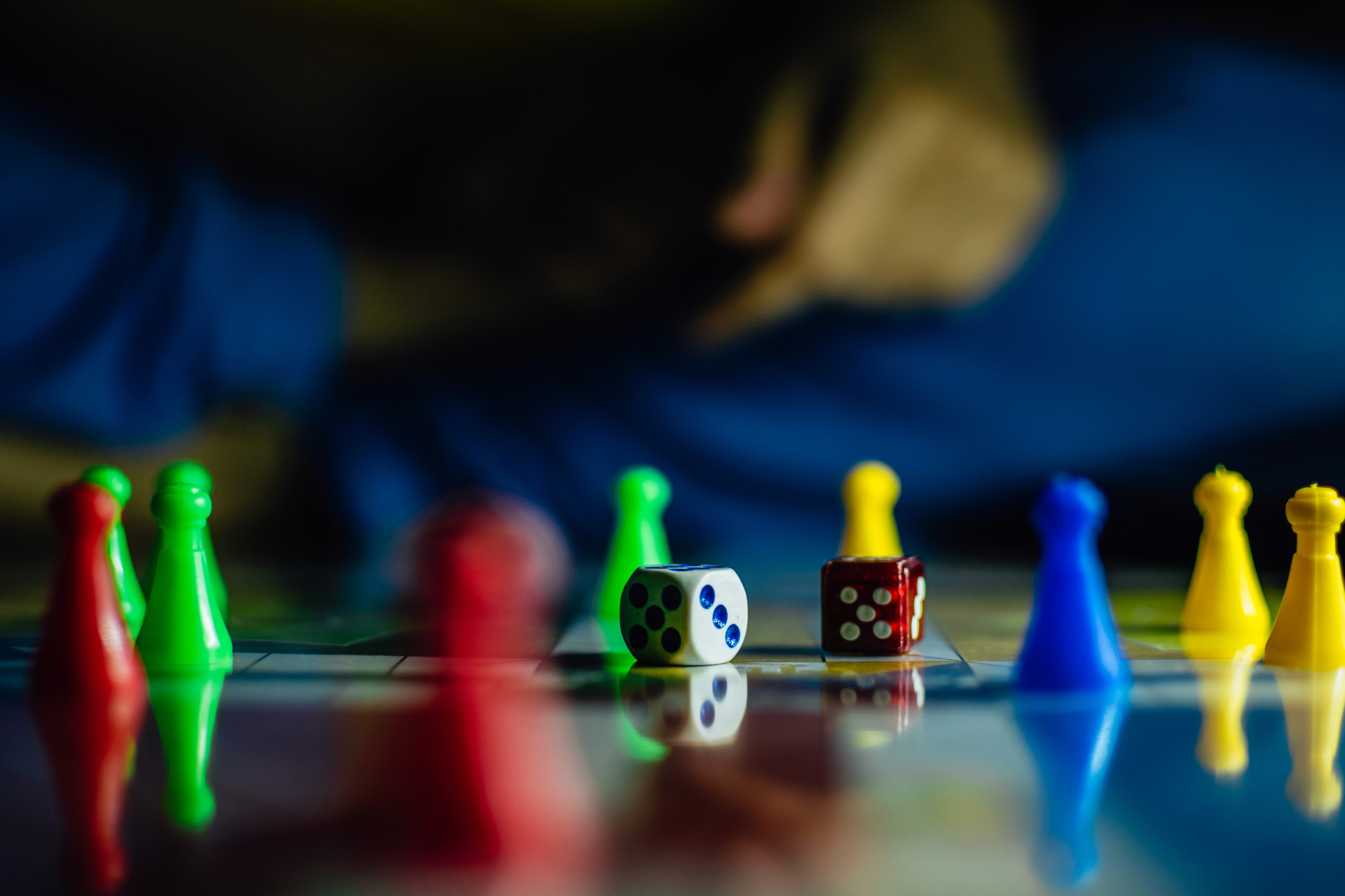 Smiling man wearing glasses and a navy shirt over a white t-shirt, standing in front of a sunlit wall with window shadows.