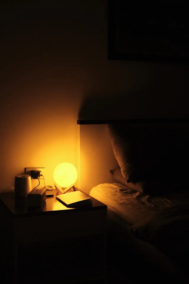 "Warm bedside lamp, book, and phone docked away on a nightstand