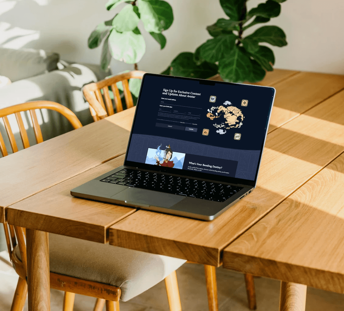 Fluid web design of a newsletter sign-up form and illustrated character card shown on a laptop in a sunlit room with wooden table and plants.
