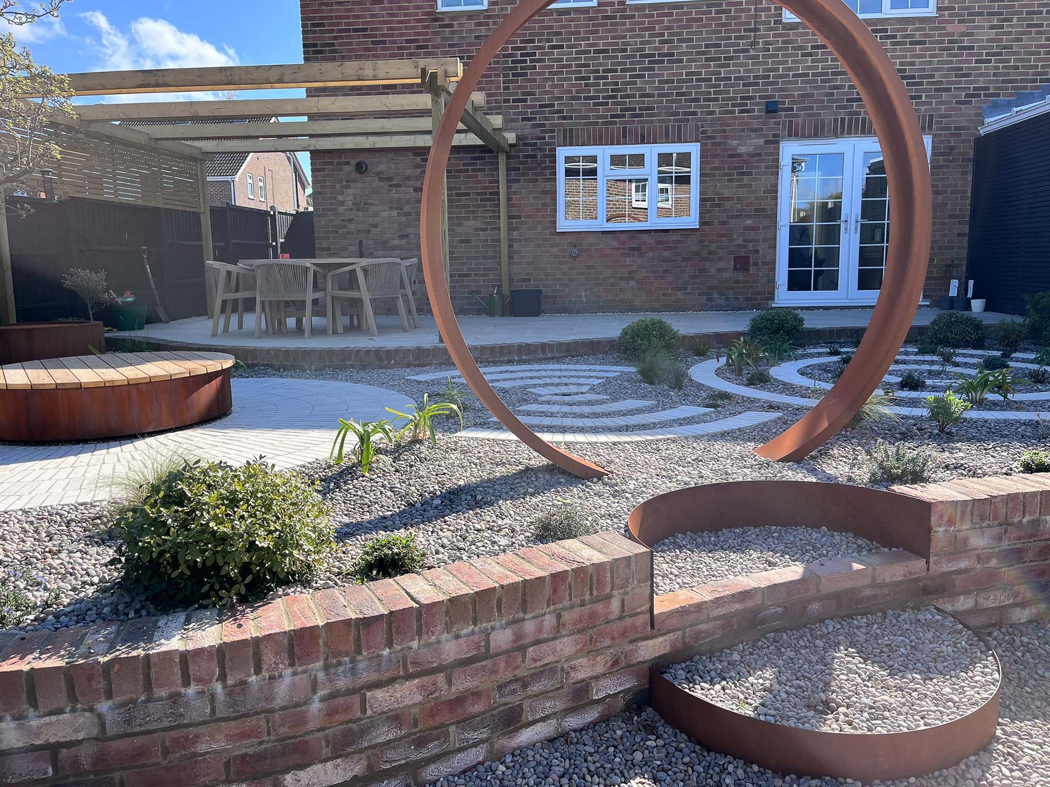 A backyard scene featuring stone pathways, plants, and a modern home in the background under a clear blue sky.