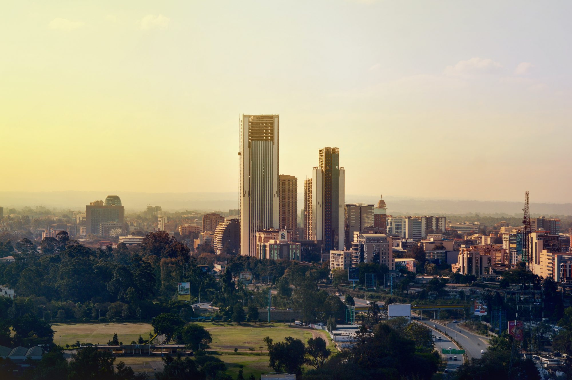 City skyline during sunrise with tall buildings silhouetted against a colorful sky and urban landscape below.