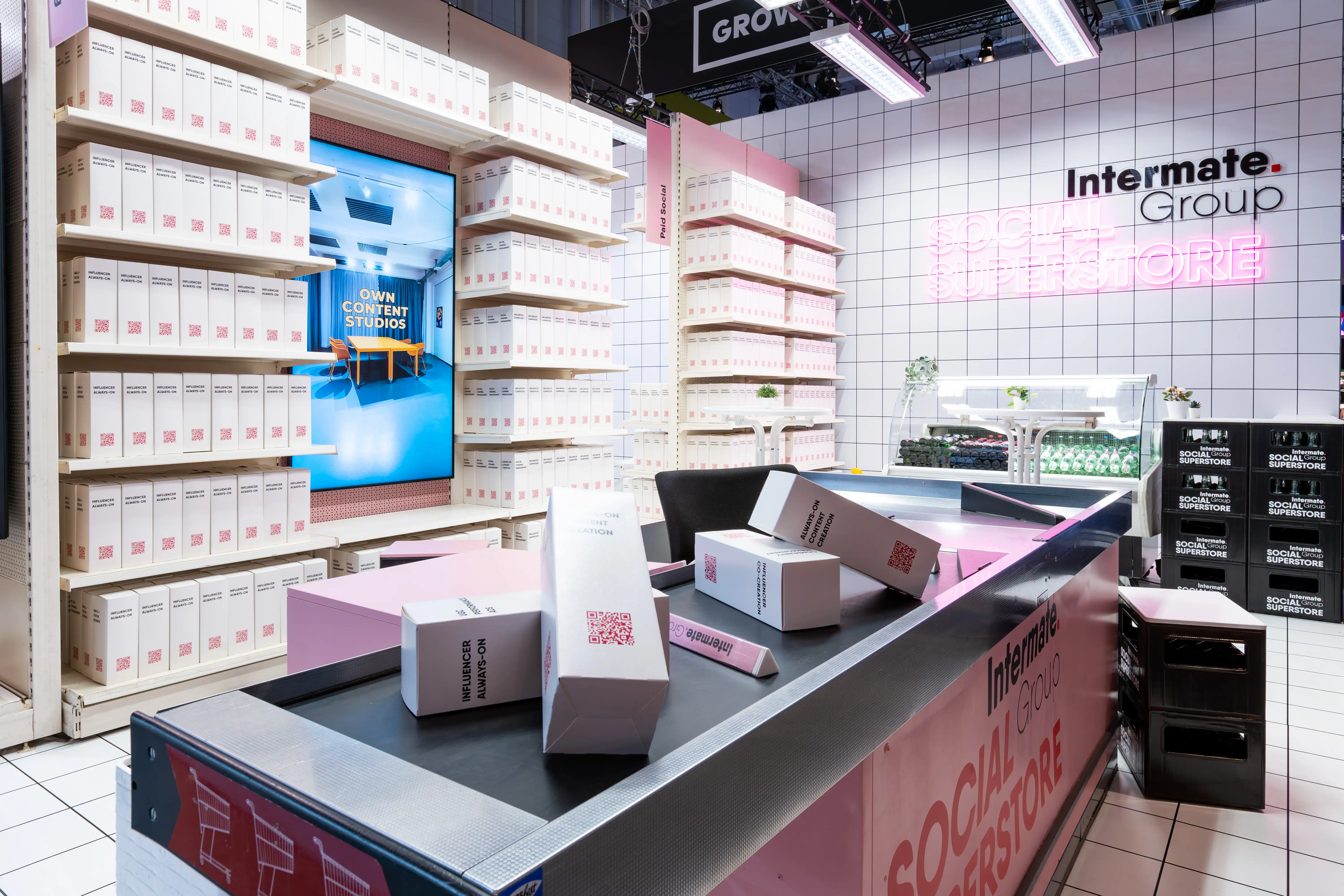 Checkout counter with conveyor belt and pink Social Superstore branding at the Intermate booth at OMR.