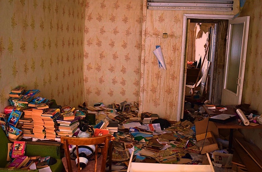 Indoor image of a home with piles of books on the floor. It is dilapidated.