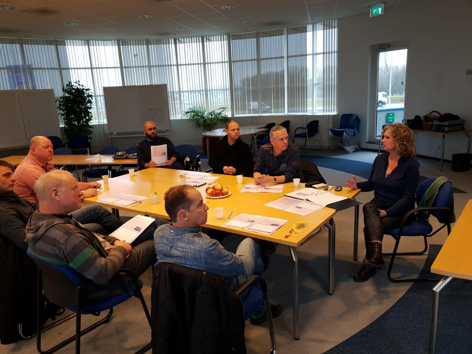 Two women sitting at a table in a modern office, one working on a laptop and the other having coffee.