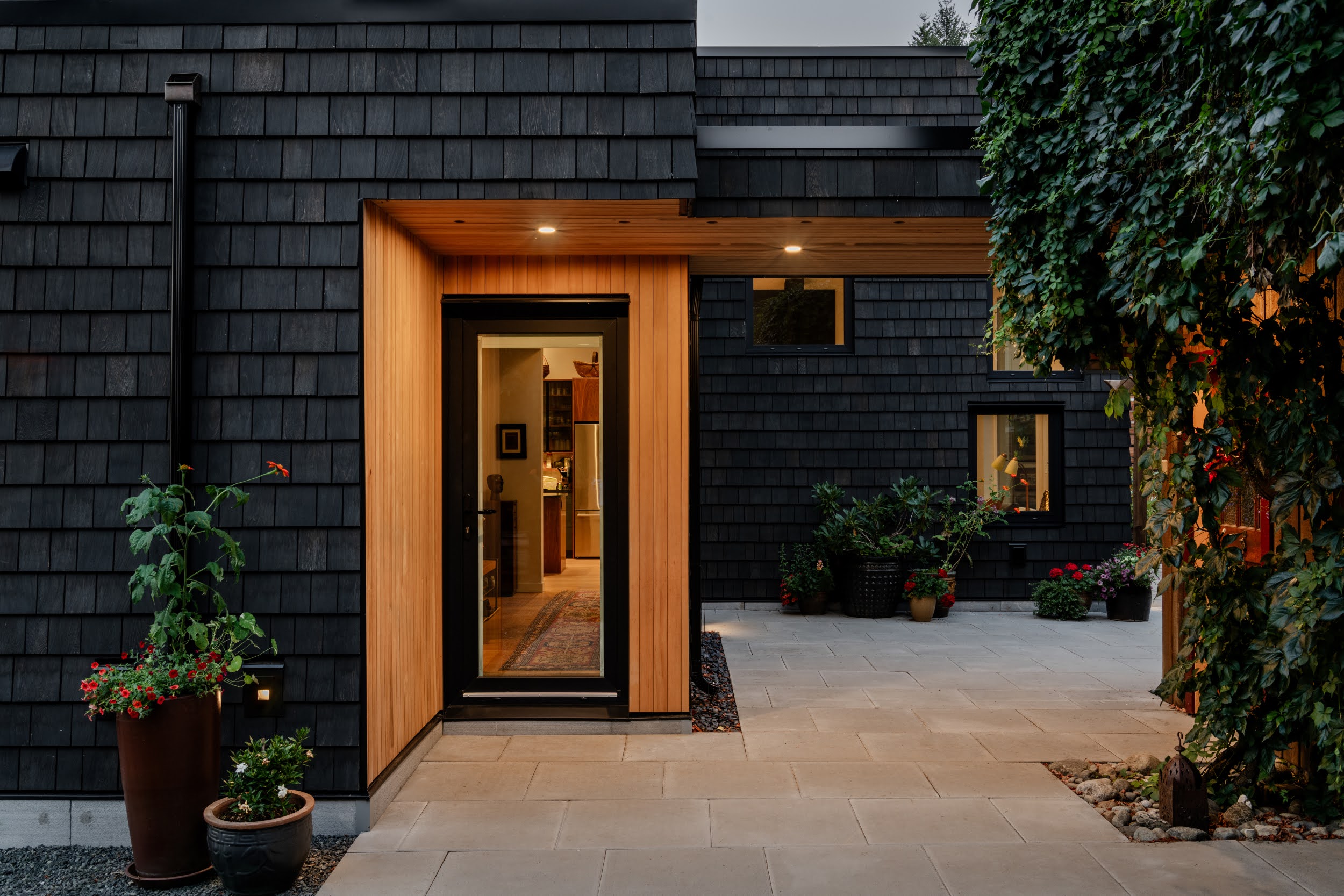A serene outdoor seating area with two chairs, surrounded by lush greenery and a glassed-in structure.