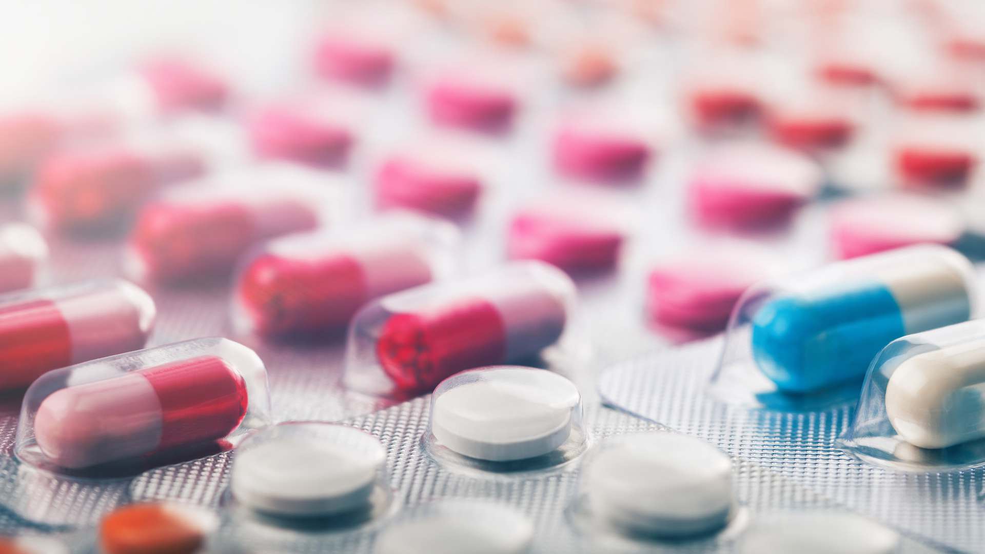 Close-up of blister packs of red, pink, blue and white capsules alongside white tablets