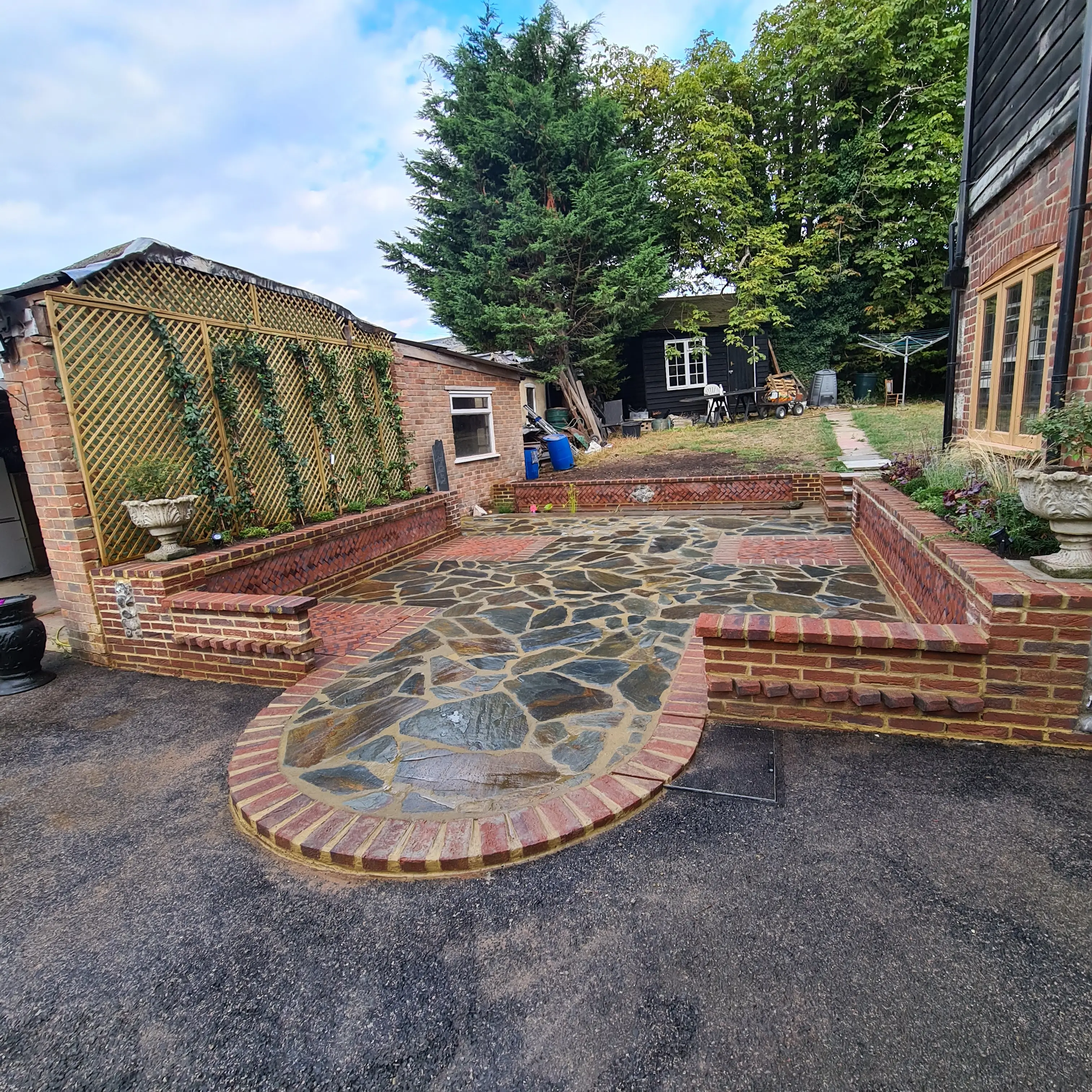 A landscaped area with stone pathways and brick borders, featuring trees and workers in the background.