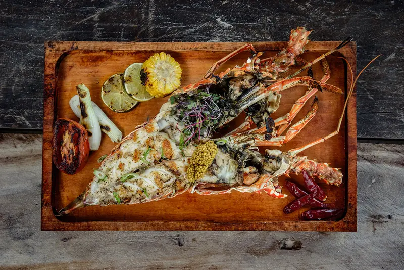 Charcoal-grilled lobster with spices and seasonings, accompanied by roasted tomato, onion, lemon, and corn at 4 Fuegos restaurant, Be Tulum.