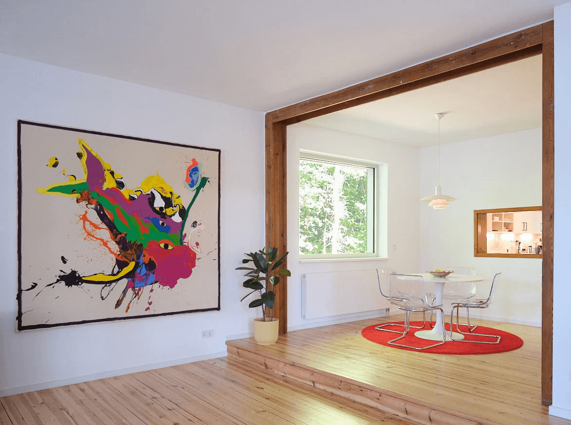 Modernes, helles Wohnzimmer auf zwei Ebenen, mit Wanddurchbruch, eines großen Gemälde an der einen Wand und einer Sitzecke auf rotem Teppich.