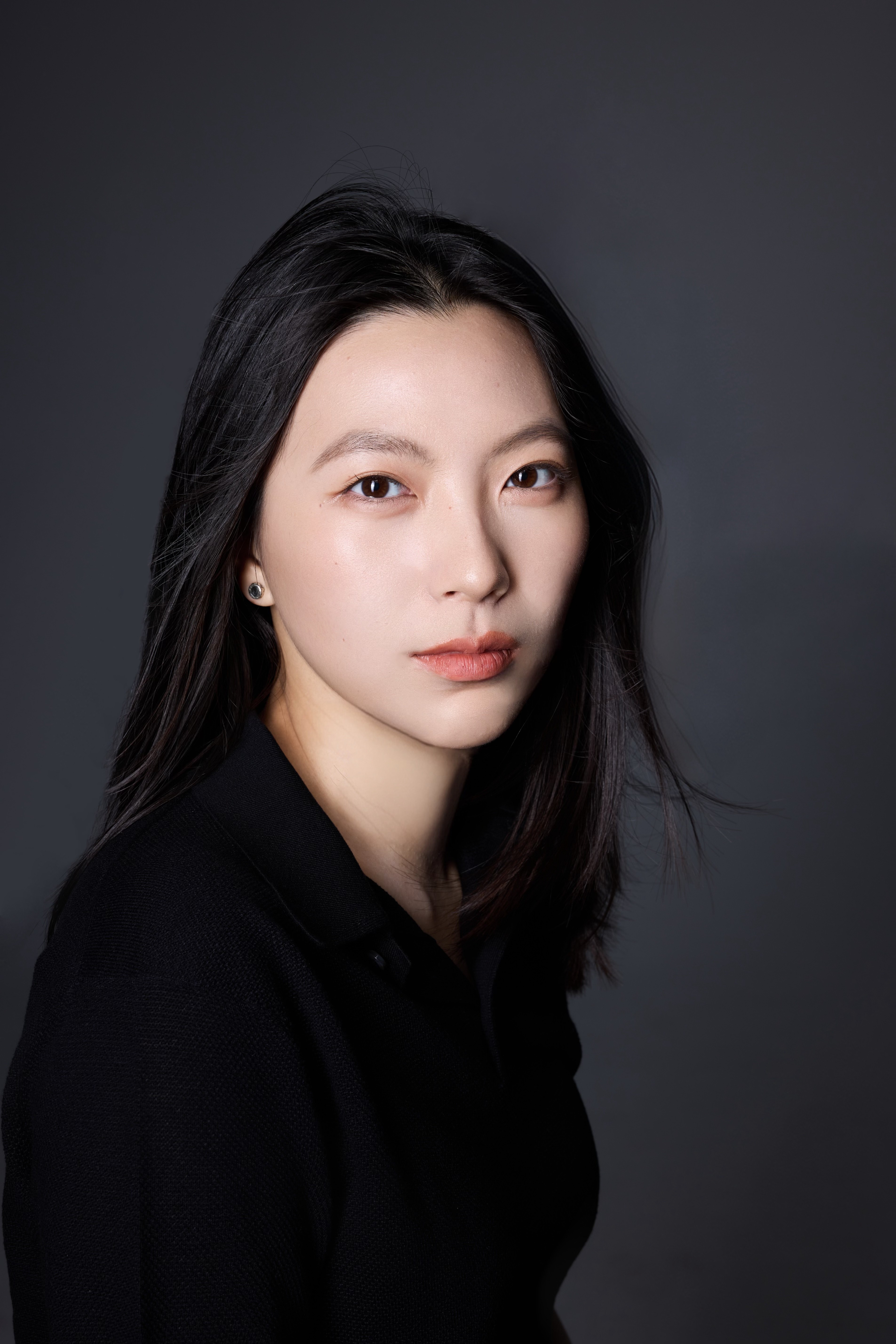 A thoughtful young person with dark hair gazes to the side, captured in soft black and white lighting.