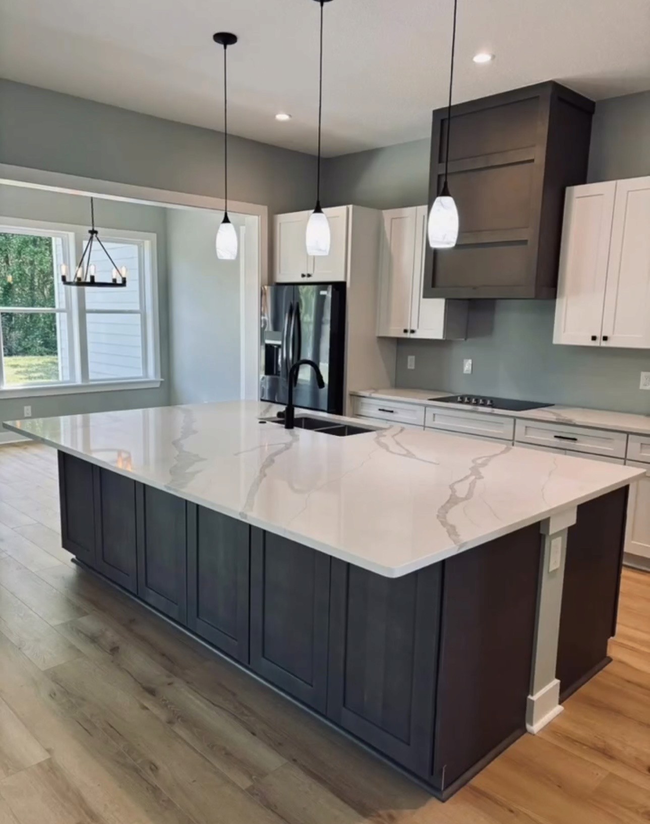 Luxury kitchen with dark island, white quartz countertop, pendant lights, wood range hood, and natural window light