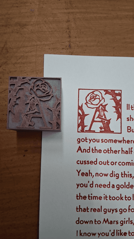 The 3D printed A dropcap next to its print on the verse.
