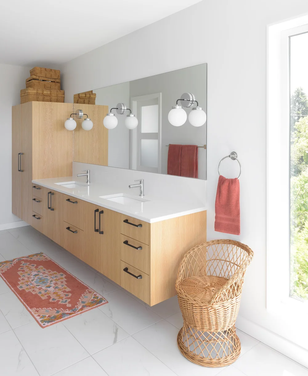 Modern two-story home with large glass windows, warmly lit interiors, and a balcony. Surrounded by trees and a manicured lawn at dusk. Cozy ambiance.