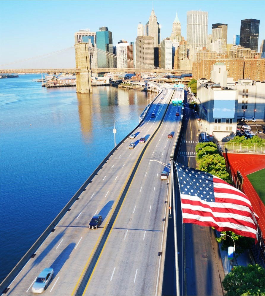 Smiling young woman with long hair standing against a dark green background, holding a finger to her chin.