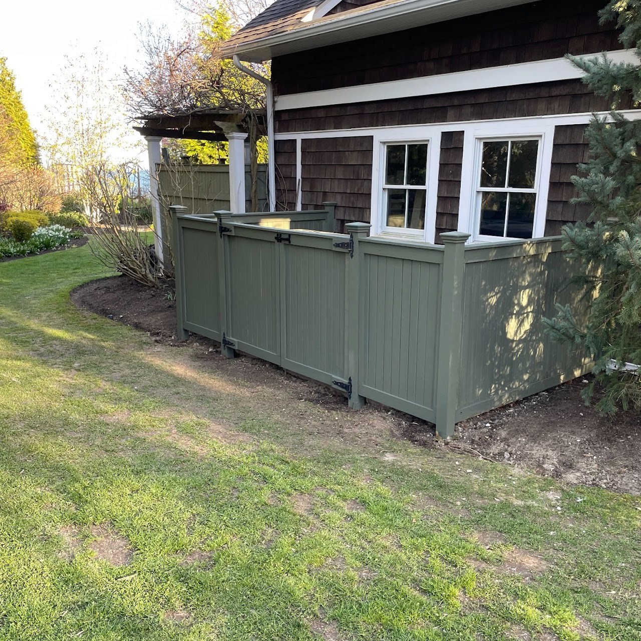 New green vinyl privacy fence enclosing equipment beside shingled home