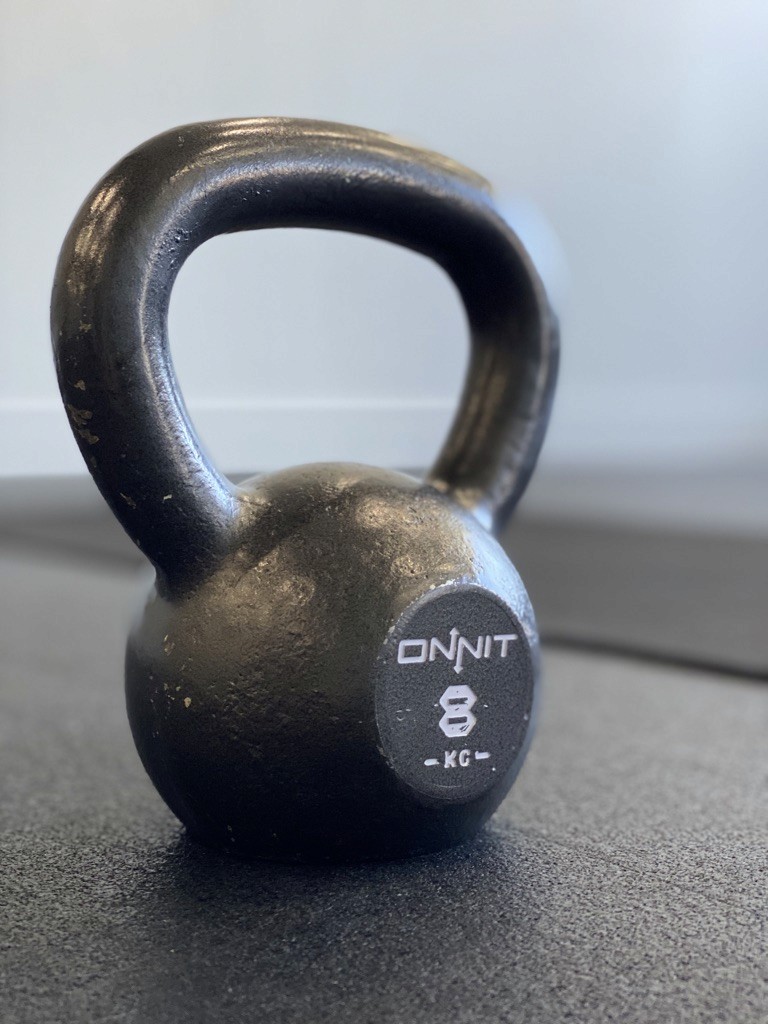 A black, cast-iron kettlebell weighing 8 kilograms rests on a rubber gym floor, highlighting fitness equipment and strength training.
