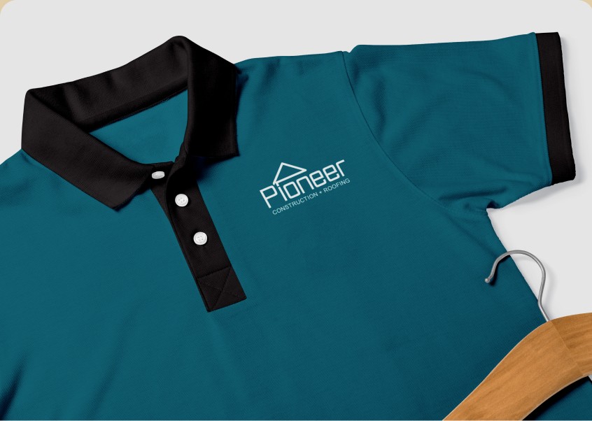 Teal polo shirt with Pioneer Construction + Roofing embroidered logo displayed on a hanger.