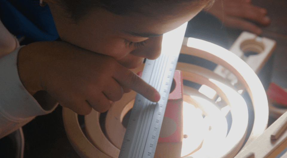 Niño concentrado usando una regla en un juguete de construcción de madera, mostrando aprendizaje práctico y exploración