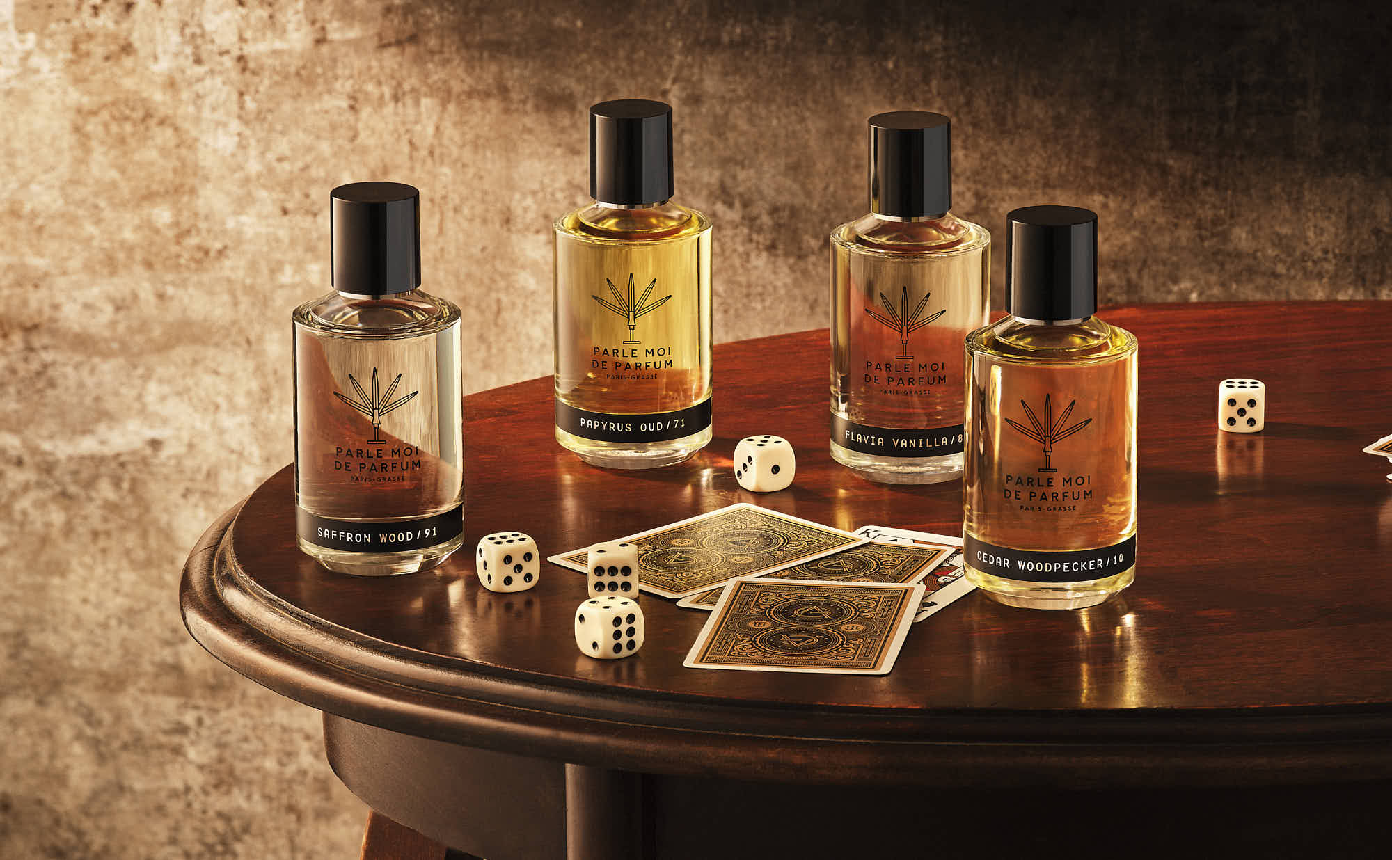 Four bottles of cologne are elegantly arranged on a wooden surface against a textured wall background.