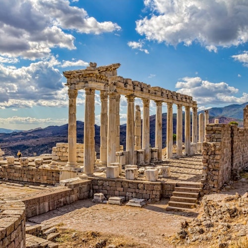 在部分多云的天空下，背景是群山的古代遗迹，遗迹中有石柱和拱门。