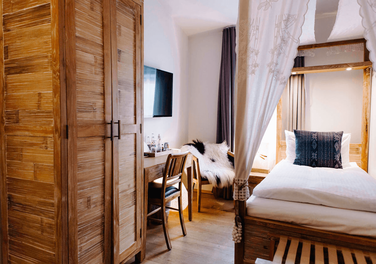 Hotel bedroom with wooden furniture, a comfortable bed, a small workspace, and soft natural light