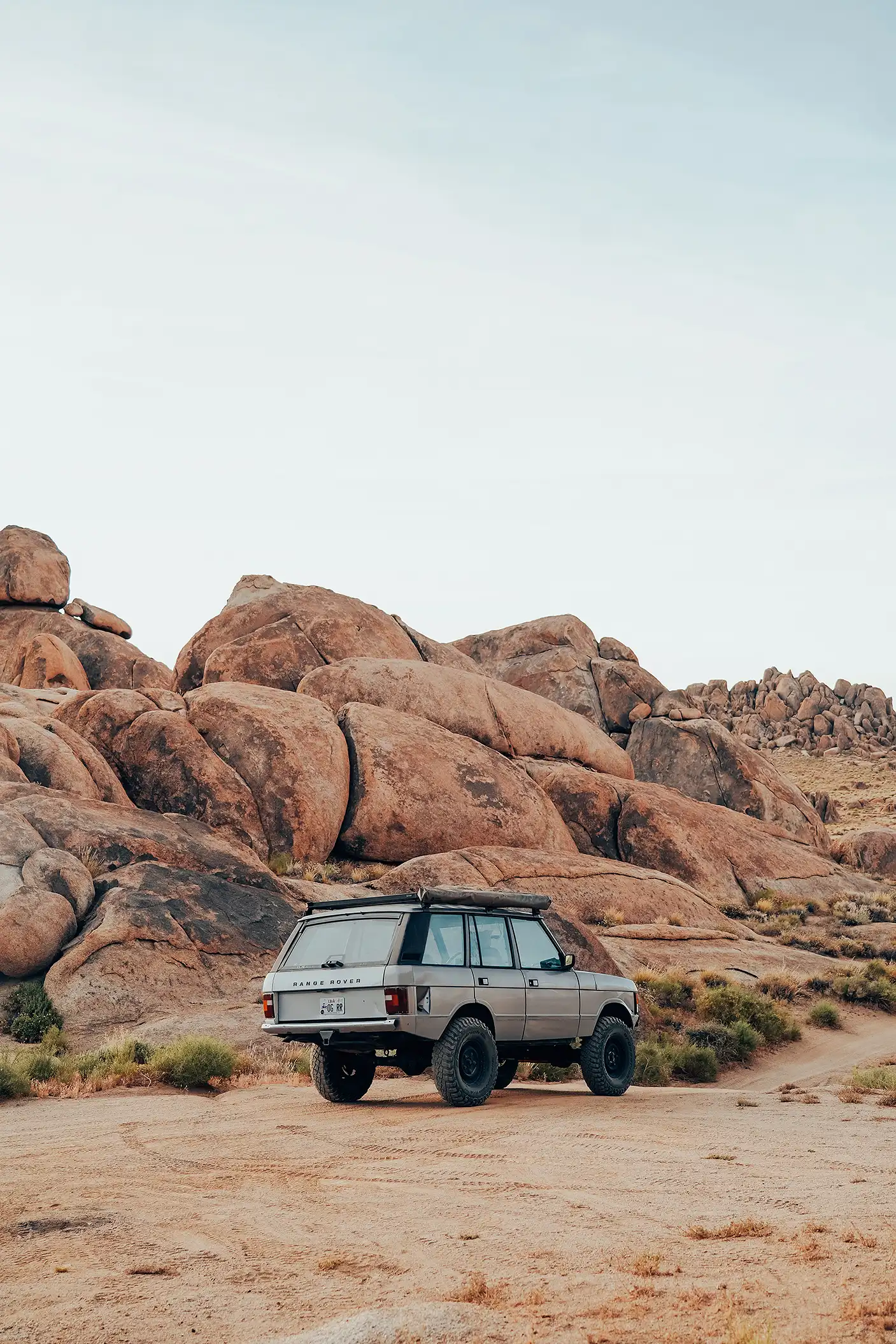 A silver Range Rover SUV parked in the desert, with large rocks and boulders in the background.