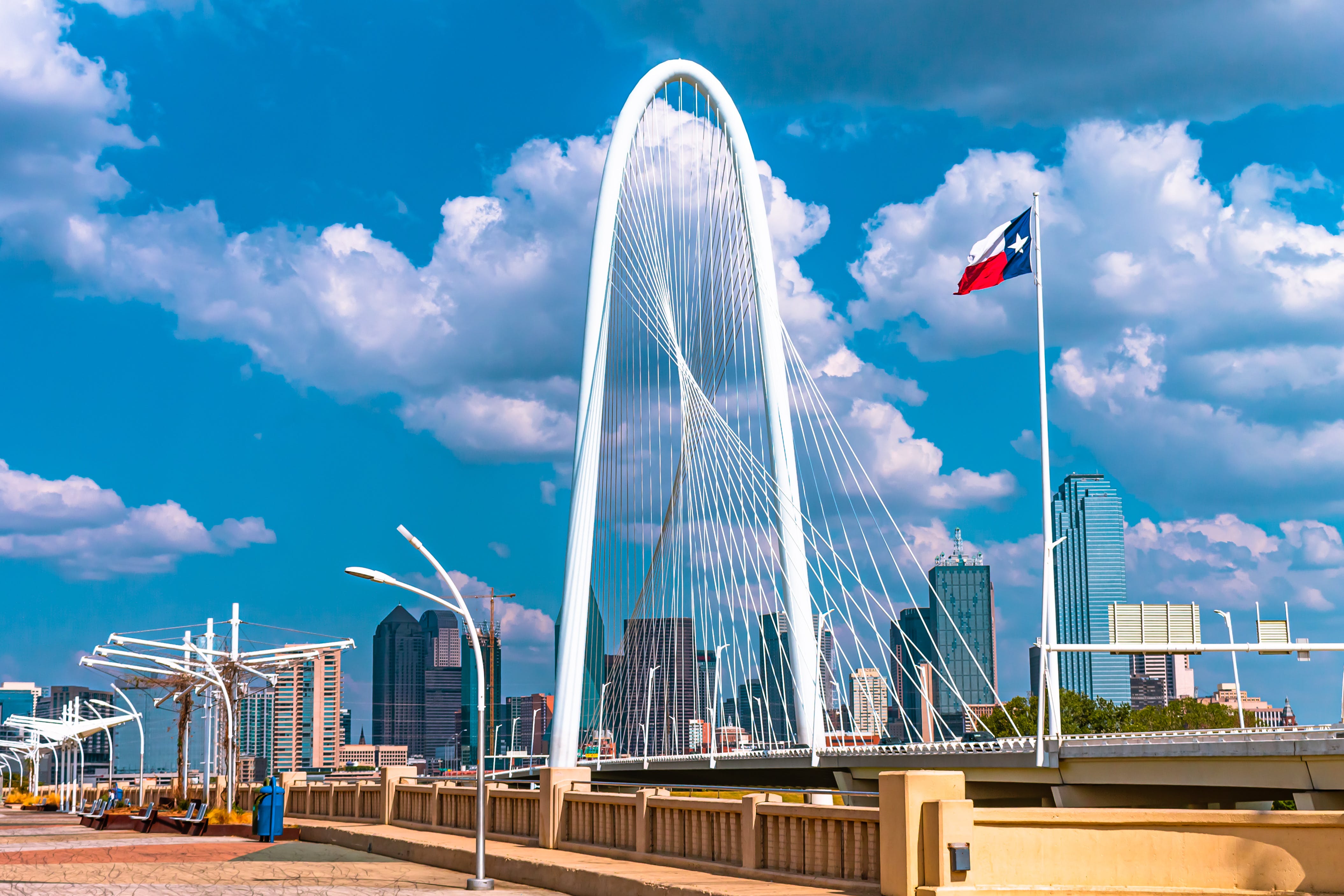 The Dallas arched white bridge against a clear blue sky with the Texas flag waving beside the bridge