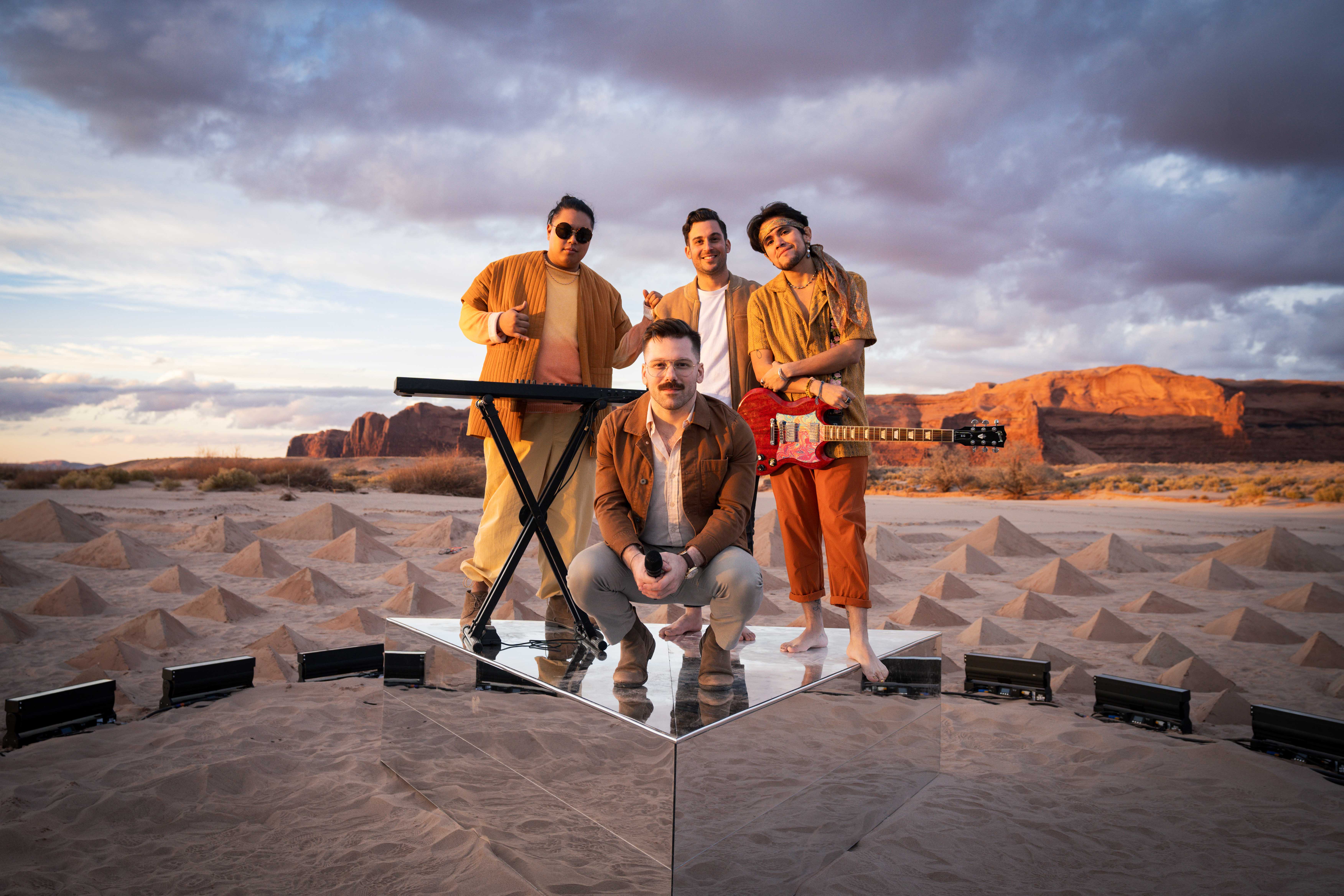 The band ARIZONA and director Owen Brown standing on a stage made of mirrors surrounded by pyramids made of sand