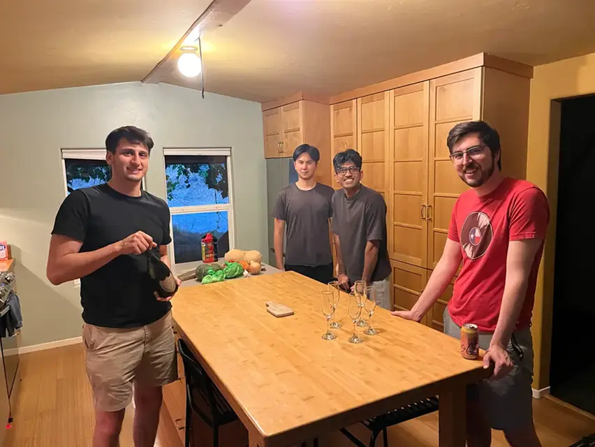 Four men standing around a wooden kitchen island with glasses and drinks.