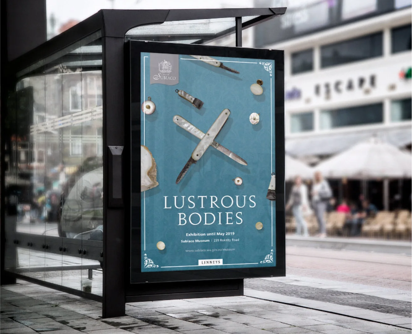 Professional street furniture advertising for Subiaco Museum, showcasing the blue 'Lustrous Bodies' exhibition poster mockup in an urban bus shelter.