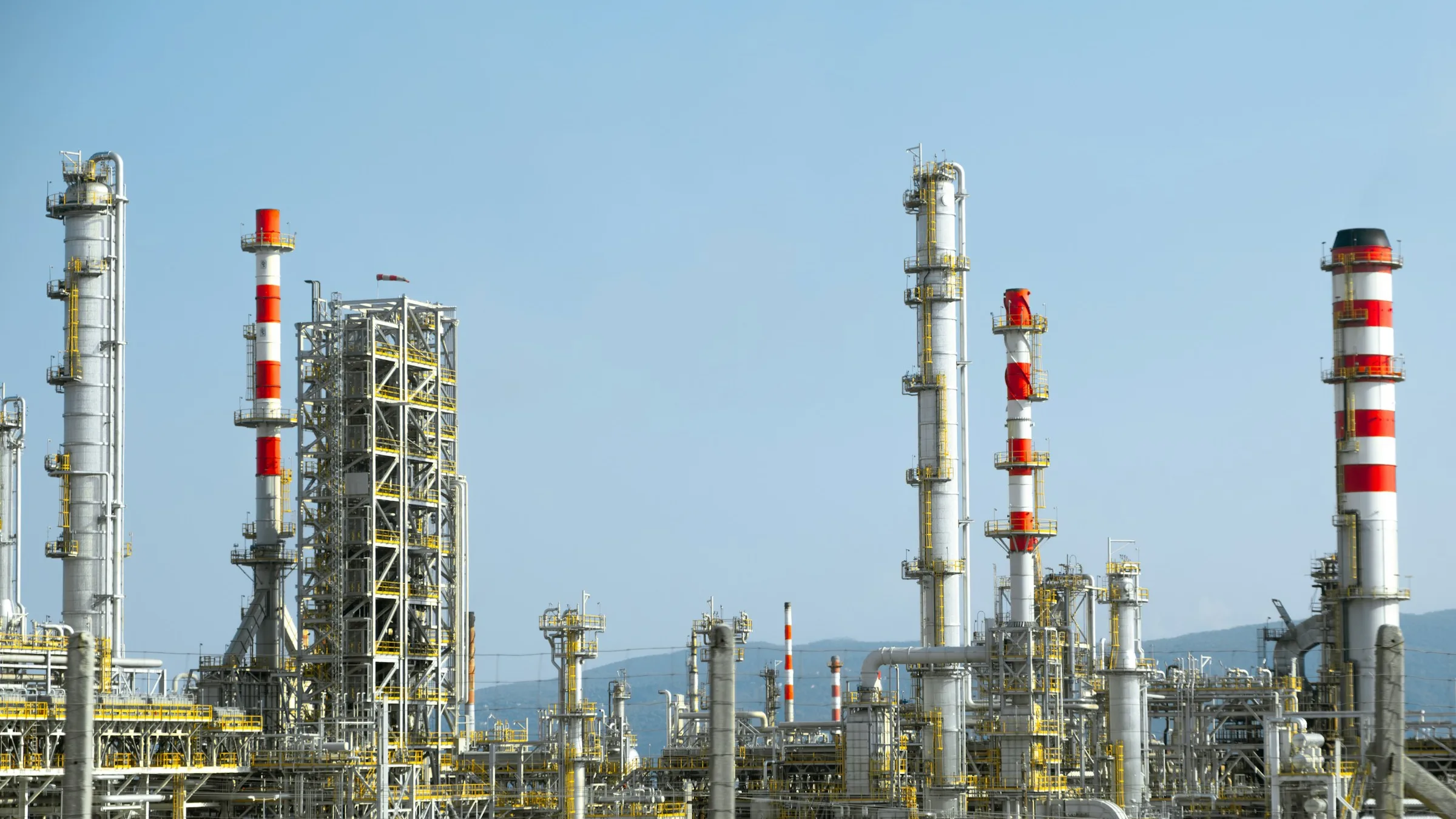 Industrial plant with tall red and white stacks, distillation columns and process piping under a blue sky