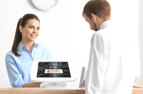 two staff members talking beside a sign in tablet