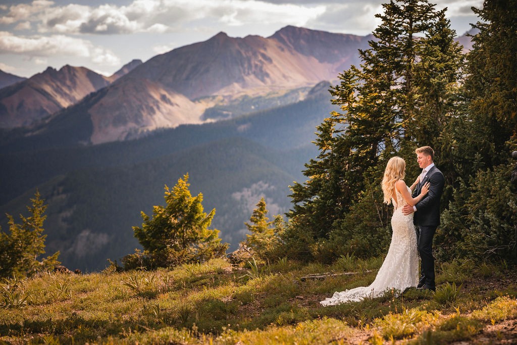 Newlyweds standing together on a sunlit mountainside