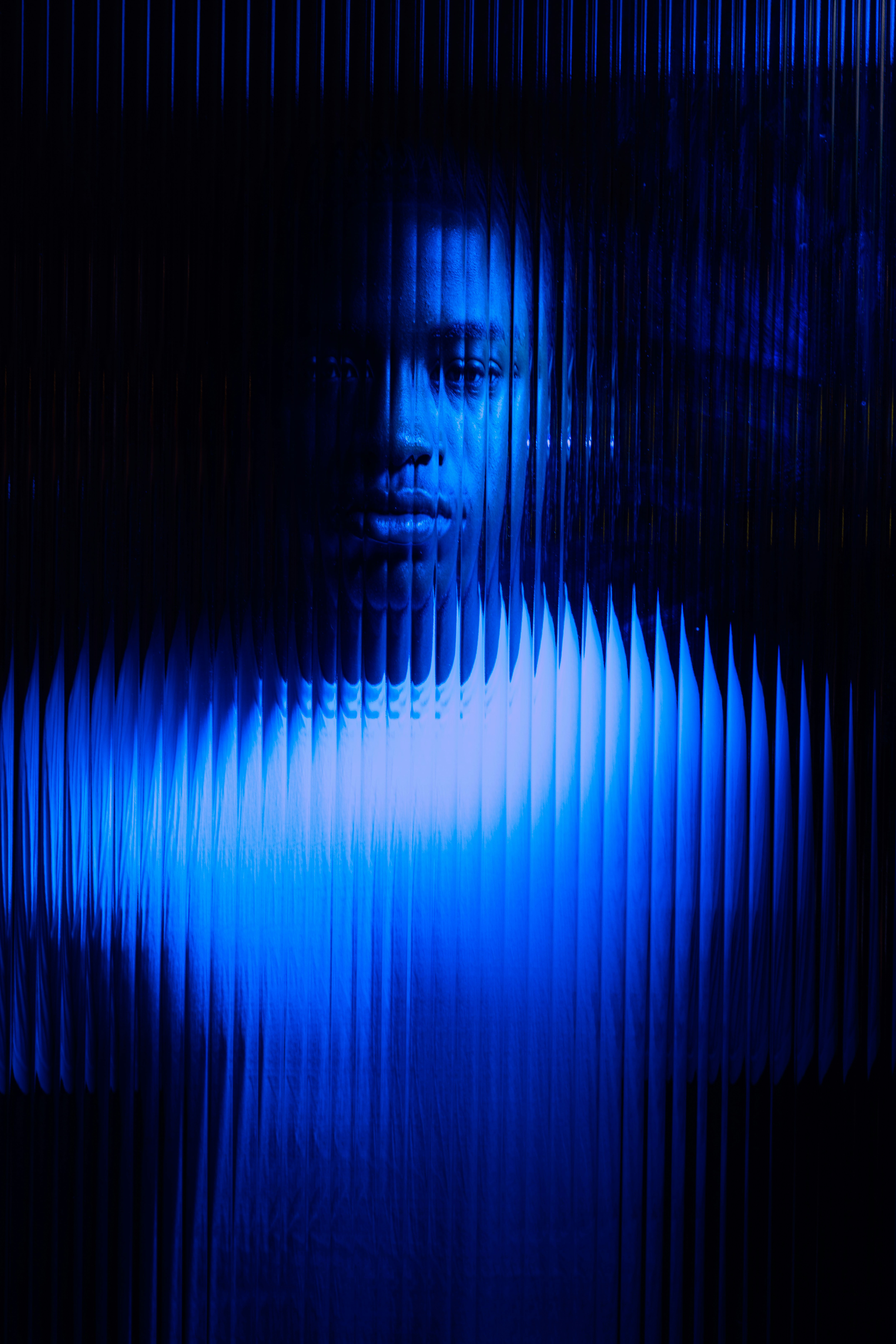 A figure is partially illuminated in blue light against a dark background, creating a haunting, ethereal effect.